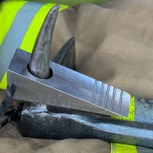 May include: A silver metal wedge with a pointed end and a textured surface. The wedge is resting on a black metal object. The text "The Truckman" is visible in the background.