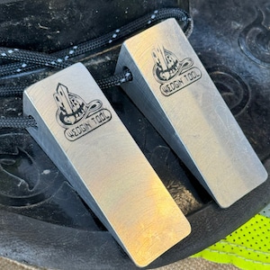 May include: Two silver metal wedges with the text "WEDGIN' TOOL" engraved on them. The wedges are on a black surface and the text "The Mini's" is above them.