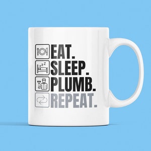 May include: White ceramic mug with a black and grey design. The mug has a handle and says "Eat. Sleep. Plumb. Repeat."