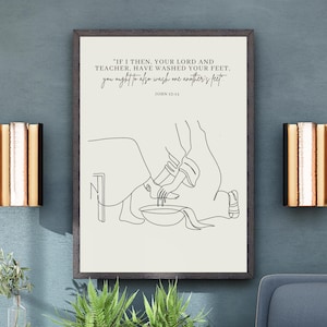 Op de afbeelding: Een ingelijste prent met een minimalistische lijntekening die een bijbelse scène uitbeeldt. De tekst luidt: 'Als Ik dan, uw Heer en Meester, uw voeten gewassen heb, behoort u ook elkaars voeten te wassen.' De prent hangt aan een blauwe muur.