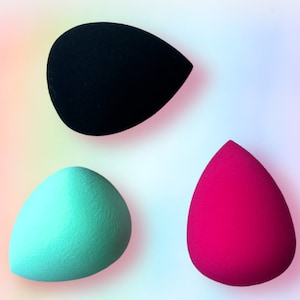 May include: Three makeup sponges in different colors: black, teal, and pink. The sponges are shaped like teardrops and are made of a soft, porous material.