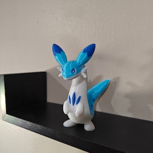 Puede incluir: Una figurita impresa en 3D de color azul y blanco de una criatura m&iacute;tica con cuello largo y cola. La criatura tiene orejas azules y un patr&oacute;n azul en su cuerpo.