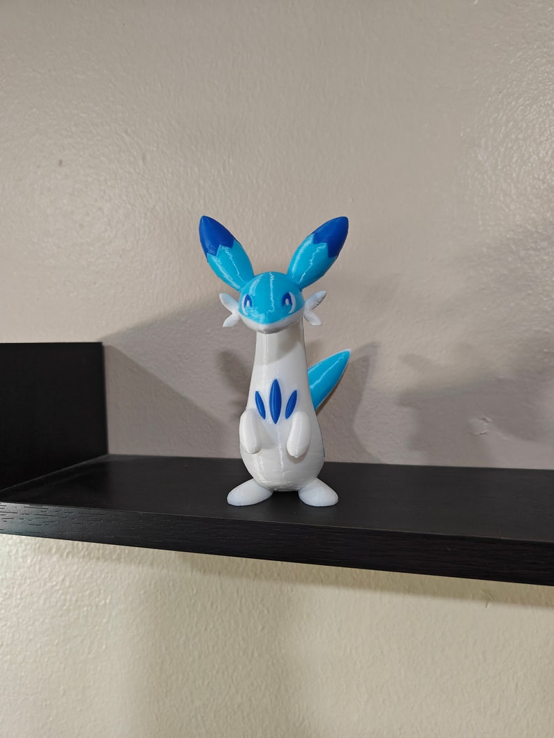 Puede incluir: Una figura de un personaje de Pokemon impresa en 3D en blanco y azul. El personaje tiene un cuello largo, un cuerpo blanco, orejas azules y una cola azul.