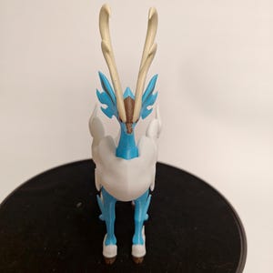 May include: A blue and white Pokemon figurine with large antlers. The figurine is standing on a black surface.