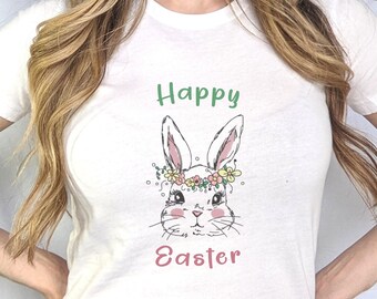 May include: White t-shirt featuring a hand-drawn bunny wearing a floral crown, with the words "Happy Easter" in green and pink. The design is centered on the front of the shirt.
