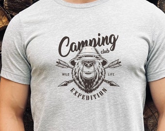 Puede incluir: Una camiseta gris con un gráfico vintage de un oso con un sombrero y el texto "Camping club, Wild life, Expedition".