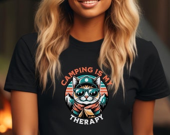 May include: A black t-shirt with a graphic of a cat wearing sunglasses and a hat. The text on the graphic says "Camping is my therapy".