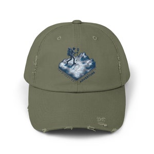May include: Olive green distressed baseball cap with a blue and white graphic of a hiker on a topographic map. The word "ADVENTURE" is printed below the graphic. The cap has a pre-worn appearance.