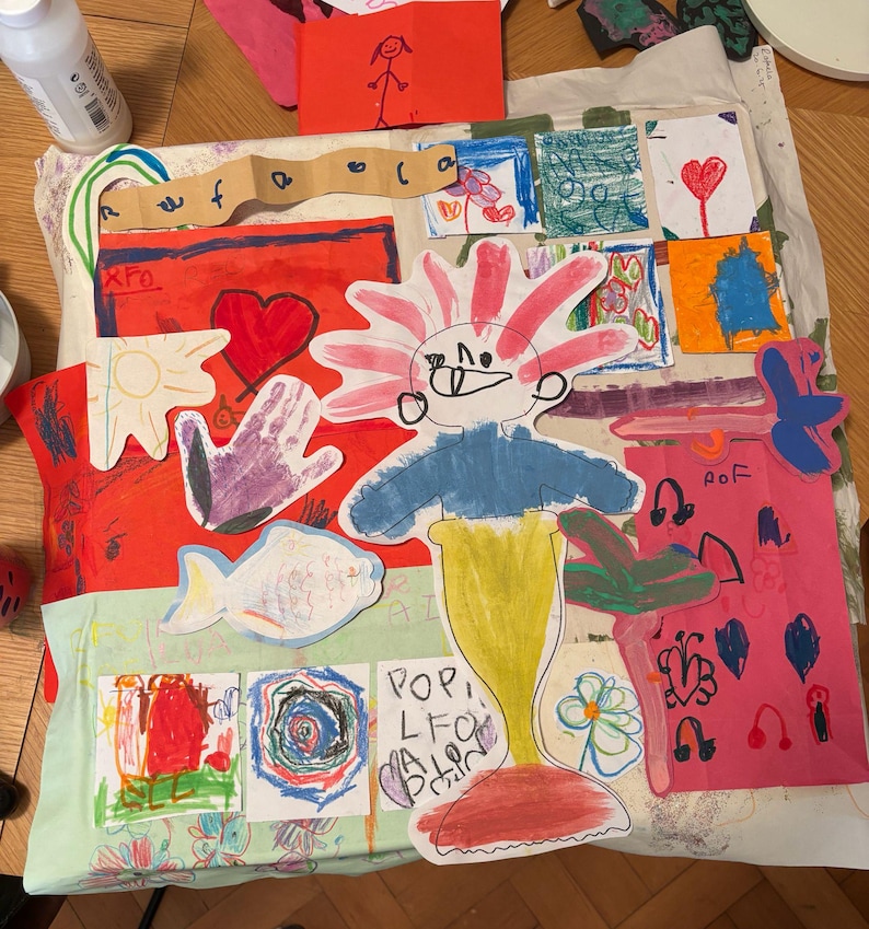 May include: A collage of colorful children's drawings on paper, featuring a central figure with a pink spiky head, blue torso, and yellow tail. Surrounding elements include a red heart, a purple handprint, a fish, and various small sketches.