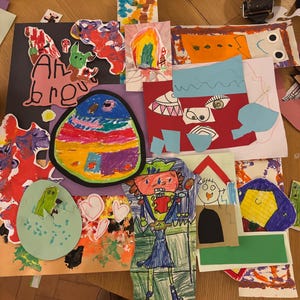 May include: A collection of colorful children's artwork featuring various drawings and paper cutouts. The collage includes a large oval with rainbow stripes, a figure in a blue outfit, a green creature in an egg, and abstract shapes in red, orange, and blue.