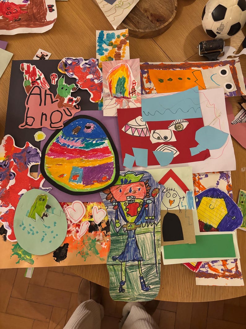 May include: A collection of colorful children's artwork featuring various drawings and paper cutouts. The collage includes a large oval with rainbow stripes, a figure in a blue outfit, a green creature in an egg, and abstract shapes in red, orange, and blue.