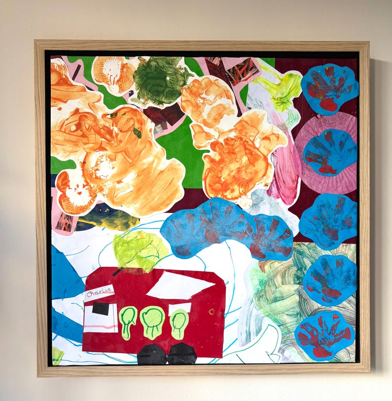 May include: A framed mixed-media collage featuring a red bus cutout with the name Charlie printed on it, surrounded by abstract orange paint blobs, green shapes, and a vertical column of blue handprint cutouts on a white and dark red background.