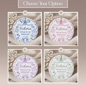May include: Four round bridesmaid proposal ornaments in blue, pink, purple, and green. Each ornament features a bow, the name "Victoria", and the text "Will you be my Bridesmaid?" with the date 10.07.2025.