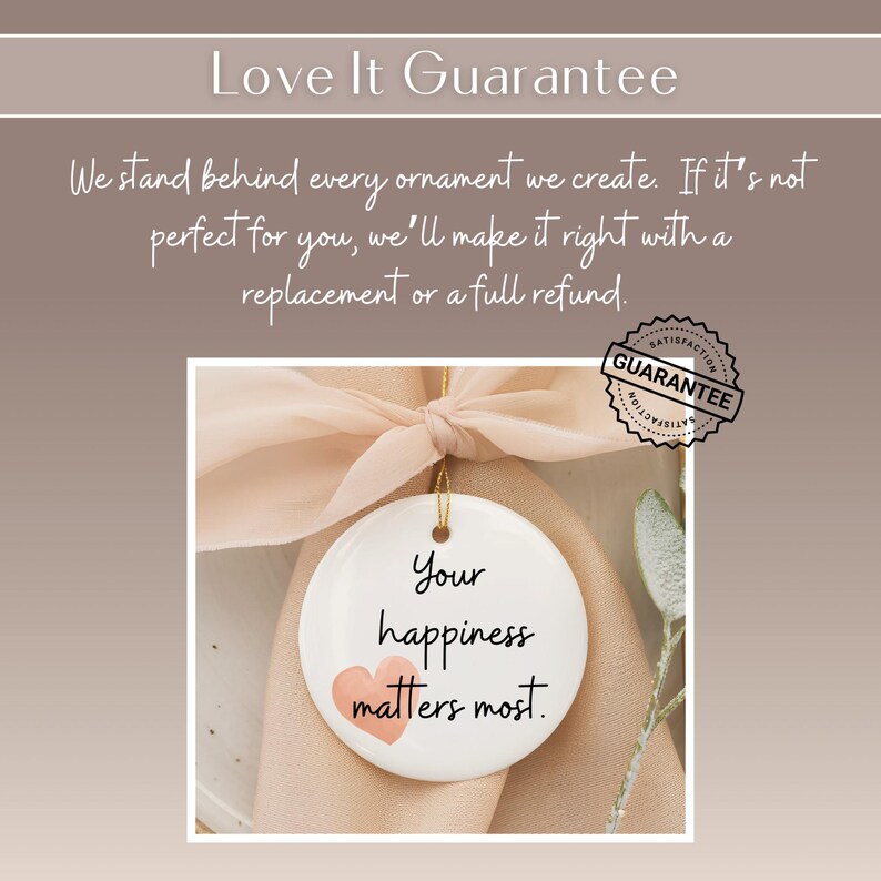 May include: A white, round ornament with the text "Your happiness matters most" and a pink heart. The ornament hangs from a gold string and a peach-colored ribbon. A "Satisfaction Guarantee" seal is visible.