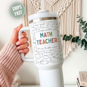 May include: White insulated tumbler with a large handle, featuring a design for a math teacher. The tumbler is covered in mathematical equations and formulas. The words "MATH TEACHER" are displayed in colorful letters, with the name "Mrs. Robinson" below.