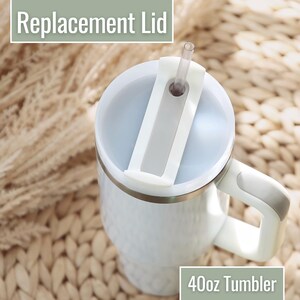 May include: A white 40oz tumbler with a handle and a replacement lid featuring a white sliding closure and a clear straw. The text Replacement Lid and 40oz Tumbler is visible in the image. The tumbler has a smooth, cylindrical body.