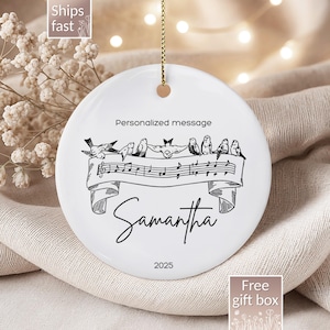 May include: White ceramic ornament with a gold string, featuring a black and white illustration of birds perched on musical notes. The ornament includes the text "Personalized message", "Samantha", and "2025".