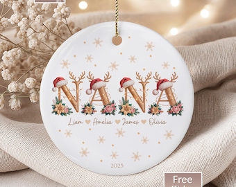 May include: White ceramic Christmas ornament with the word "NANA" in a festive design. Each letter is decorated with a Santa hat, reindeer antlers, and floral accents. Names of loved ones are below the word, with the year 2025.