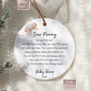 May include: A white ceramic ornament with a gold string for hanging. The ornament features the text "Dear Mommy" and a poem about a baby. A light brown bow graphic is at the top. The year 2025 is printed at the bottom.