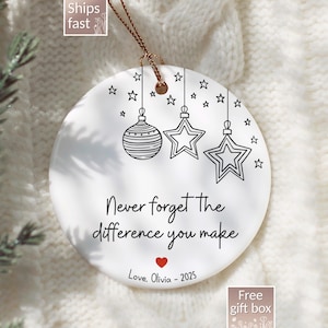 May include: White ceramic Christmas ornament with black line art of stars and hanging ornaments. The text reads "Never forget the difference you make" with a heart and "Love, Olivia - 2025". Includes a gold string for hanging.