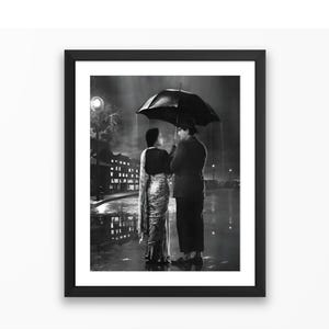 Könnte beinhalten: Schwarz-Weiß-Druck in einem Rahmen, der ein Paar unter einem Regenschirm im Regen zeigt. Die Frau trägt einen Sari, der Mann einen Anzug und einen Hut. Die Szene spielt auf einer nächtlichen Stadtstraße mit Reflexionen.