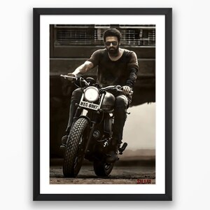 May include: A man wearing sunglasses and a black t-shirt rides a black motorcycle. The motorcycle has a license plate that reads "MEC 6987". The word "Salaar" is printed in red at the bottom of the image.