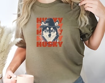 May include: A green t-shirt with a graphic of a husky dog wearing a hat and glasses. The text "HUSKY" is repeated in red letters.