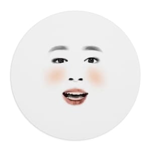 May include: A circular sticker featuring a realistic illustration of a face with dark eyebrows, dark eyes, rosy pink cheeks, and an open mouth showing teeth. The facial features are centered on a plain white background within the circular border.