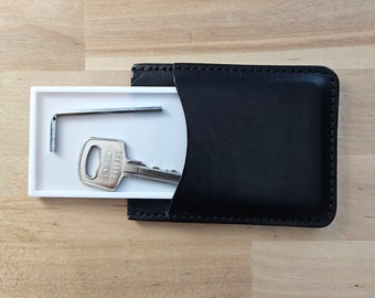 May include: A white leather key holder with a black leather flap. The holder contains a silver key and a silver Allen wrench.