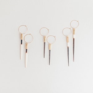 May include: Five pairs of gold hoop earrings with long, pointed, white and black feather-like dangles.