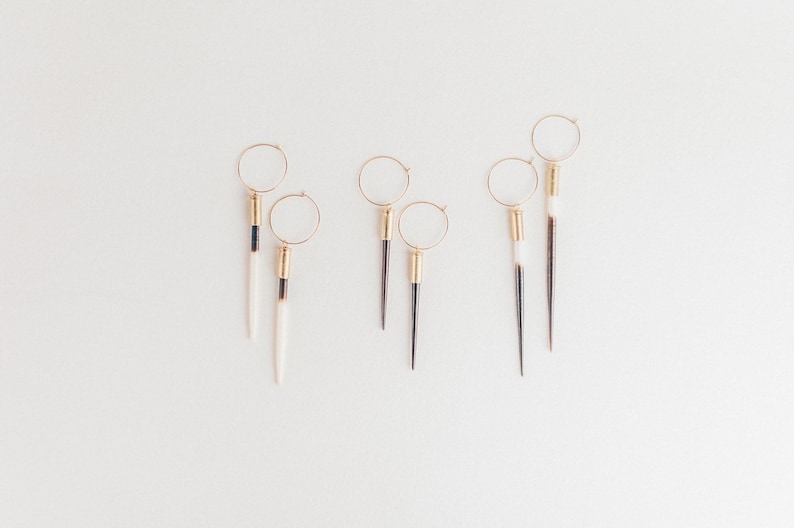 May include: Five pairs of gold hoop earrings with long, pointed, white and black feather-like dangles.