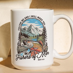 May include: White ceramic mug with a wraparound graphic featuring a fish, mountains, and trees. The text "Follow me and I will make you" and "Fishers of Men" are also displayed. The mug has a large handle.