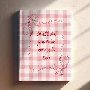 May include: A rectangular print with a pink and white gingham pattern. The print features a red ribbon border with bows and the text "let all that you do be done with love" in red script. The print is displayed on a light-colored wall.