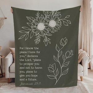 May include: Dark green throw blanket with white floral designs and text from Jeremiah 29:11. The blanket features a sunflower design and a botanical sprig. The text reads, "For I know the plans I have for you..."