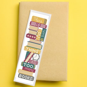 Puede incluir: Un marcapáginas blanco con una pila de libros coloridos y el texto "No existe tal cosa como demasiados libros".