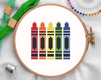 May include: A cross-stitch embroidery design of six crayons in a rainbow pattern. The crayons are red, orange, yellow, green, blue, and purple. The design is framed in a wooden embroidery hoop.