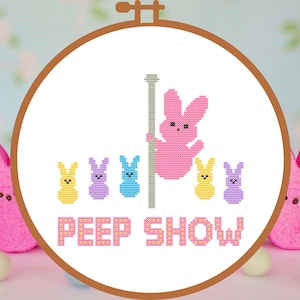 May include: A cross-stitch embroidery hoop with a white background featuring a pink Peep bunny on a pole with four other Peep bunnies in yellow, purple, blue, and yellow. The text "PEEP SHOW" is below the bunnies.