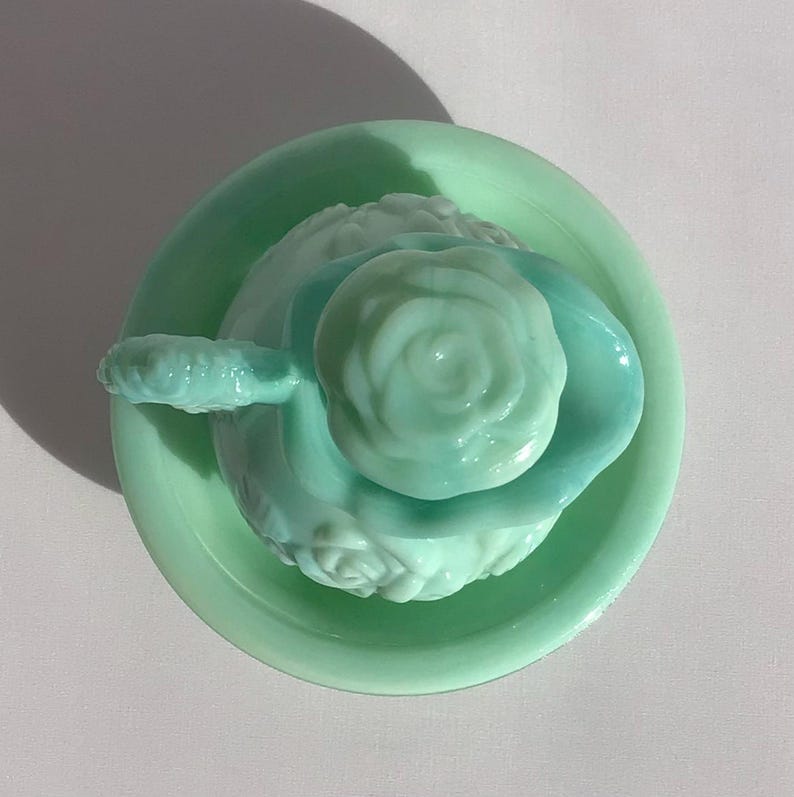 K&ouml;nnte beinhalten: Ein hellgr&uuml;nes Geschirrset im Vintage-Stil mit floralem Design. Das Set umfasst einen kleinen, runden Teller, eine Sch&uuml;ssel und ein dekoratives St&uuml;ck in Rosenform. Die Teile sind aus Glas und haben eine gl&auml;nzende Oberfl&auml;che.