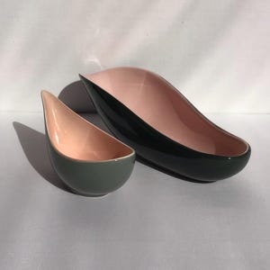 May include: Two ceramic serving bowls. The larger bowl is dark green on the outside and pink on the inside. The smaller bowl is gray on the outside and pink on the inside. Both bowls have a teardrop shape.