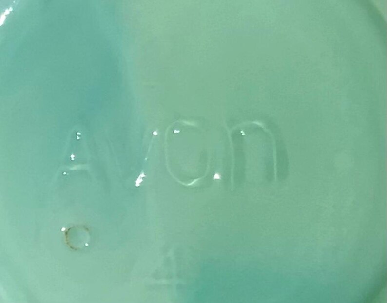 K&ouml;nnte beinhalten: Nahaufnahme einer hellt&uuml;rkisfarbenen Oberfl&auml;che mit dem gepr&auml;gten Wort "Avon". Die Buchstaben sind leicht erhaben und scheinen Teil eines gr&ouml;&szlig;eren Objekts zu sein. Die Oberfl&auml;che hat ein gl&auml;nzendes Finish.