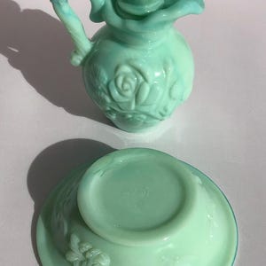 K&ouml;nnte beinhalten: Ein Vintage-Parf&uuml;mflaschen- und Schalenset aus hellgr&uuml;nem Glas. Die Flasche hat einen rosenf&ouml;rmigen Verschluss und einen Griff. Die Schale hat ein Blumendesign. Das Set stammt wahrscheinlich von Avon.