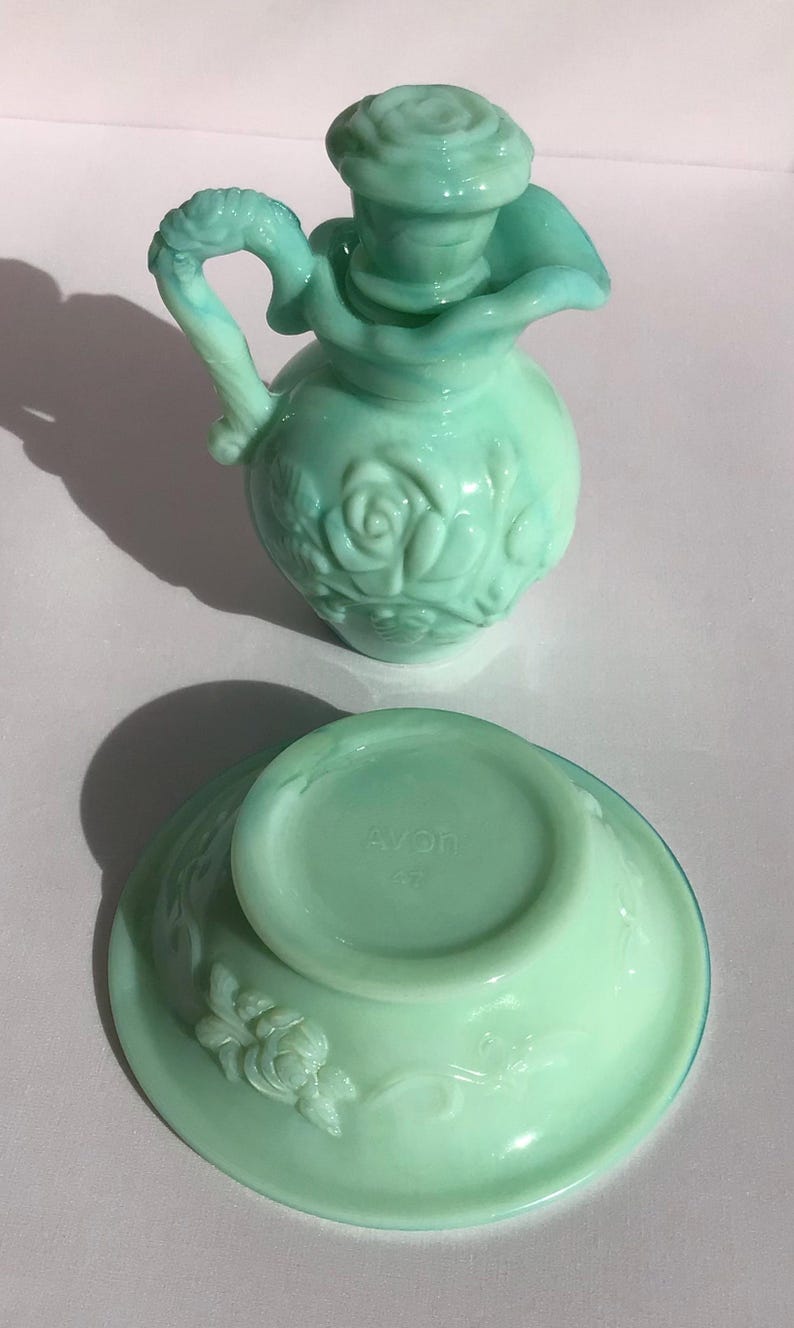K&ouml;nnte beinhalten: Ein Vintage-Parf&uuml;mflaschen- und Schalenset aus hellgr&uuml;nem Glas. Die Flasche hat einen rosenf&ouml;rmigen Verschluss und einen Griff. Die Schale hat ein Blumendesign. Das Set stammt wahrscheinlich von Avon.