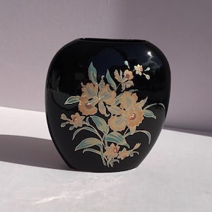 May include: Black ceramic vase with a floral design featuring yellow and gold orchids and leaves.