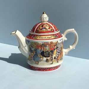 May include: A ceramic teapot featuring a colourful illustration of characters from Charles Dickens' Pickwick Papers. The lid displays a portrait of Charles Dickens, while the body shows a stagecoach scene with gold trim on the handle and spout.