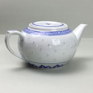 May include: A white teapot with a blue and white floral design. The teapot has a round body and a spout on the side. The lid is also decorated with a blue and white floral design.