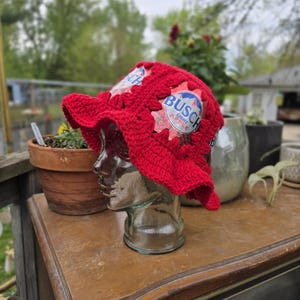 May include: Red crocheted bucket hat with a Busch Light Apple beer can label incorporated into the design.