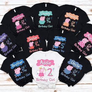 May include: A collection of black and white t-shirts featuring Peppa Pig character graphics and text. The shirts display various family titles such as Gramma, Daddy, Mommy, Grandpa, Sister, Charlie, Auntie, Brother, Uncle, and Addie with age numbers.