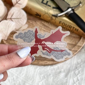 May include: A clear sticker with a red dragon flying through gray clouds. The sticker has the text "A dragon without its rider is a tragedy. A rider without their dragon is dead."