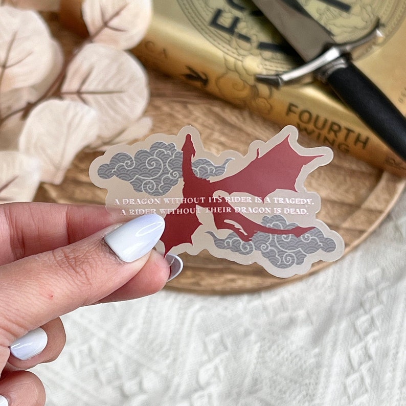 May include: A clear sticker with a red dragon flying through gray clouds. The sticker has the text "A dragon without its rider is a tragedy. A rider without their dragon is dead."