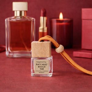 May include: A clear glass bottle with a wooden cap and an orange cord, labeled "Inspired by BACCARAT ROUGE 540 COASTAL CANDLE BAKERY." Other items include a perfume bottle, lipstick, and a lit candle, all in shades of red.